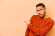 © Asier - Young hispanic man isolated on beige background smiling and pointing aside, showing something at blank space.