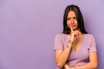 Young hispanic woman isolated on purple background looking sideways with doubtful and skeptical expression.