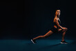 Side view of fit woman stretching legs. Caucasian female working out on black background.
