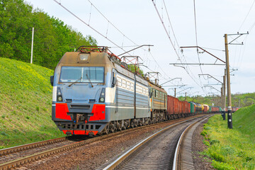 Four powerful electric locomotives pull a long heavy train to the sorting station. Spring evening lighting.