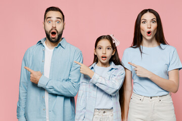 Sticker - Young shocked parents mom dad with child kid daughter teen girl in blue clothes point index finger aside on workspace isolated on plain pastel pink background. Family day parenthood childhood concept.