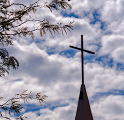 Wall Mural - Tree branches on a blurred background of a huge cross at the top of the church on a cloudy day