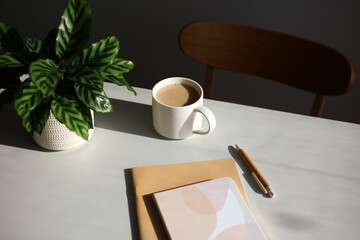 Wall Mural - Aesthetic modern home office desk table with paper notebooks, pen, cup of coffee, green plant. Feminine workspace at sunset.