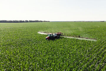 Self-propelled sprayer sprays green corn with pesticides on a photo field from a drone. The tractor sprays the grass with pesticides.