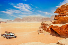 Orange Sands And Rocks Of Wadi Rum Desert With Jeeps In The Foreground, Jordan
