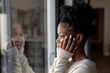 © Wavebreak Media - Close-up of serious african american young woman with hands on chin looking through window at home