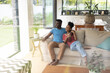 © Wavebreak Media - Smiling african american young couple looking through window while relaxing on sofa in living room