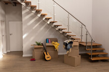 Stack Of Cardboard Boxes With Guitar, Books And Clothing By Staircase In New Empty House, Copy Space