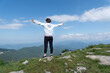 Backview of girl with hands up standing on peak of mountains looking on blue sky and mountain landscape. Freedom and victory concept