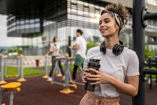 Caucasian Woman Taking A Brake During Outdoor Training In The Park Outdoor Gym Resting On The Bars With Supplement Shaker In Hand Drinking Water Or Supplementation Happy Smile Copy Space