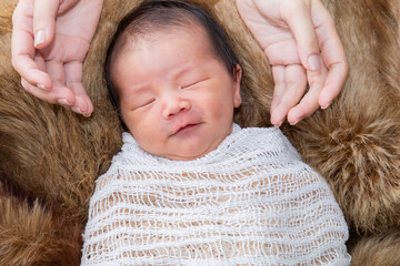 Wall Mural - Asian little newborn baby deeply sleeping wrapped in thin white clothwith happy and safe on brown wool blanket with touching of mother's care. Mom touch adorable infant with love and tender.