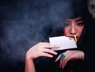 Beautiful serious mysterious woman in the darkness holding the burning tarot cards for the fortune teller read future.