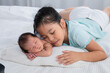 Cute Asian big sister and newborn baby sleep on bed, Girl and adorable infant lying on white bed at home. sister and brother spend time together. Toddler deeply sleeping with safe and relax.