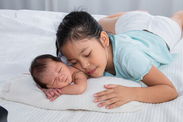 Wall Mural - Cute Asian big sister and newborn baby sleep on bed, Girl and adorable infant lying on white bed at home. sister and brother spend time together. Toddler deeply sleeping with safe and relax.