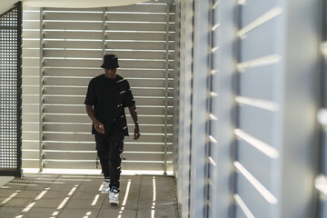 Wall Mural - Young cool black male in a street style outfit posing in a room with blinds