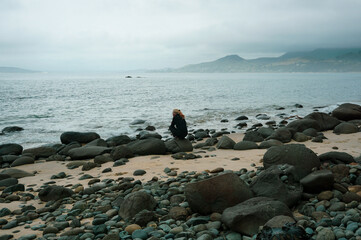 Wall Mural - A woman sitting on the rock at Waimamaku Coast in New Zealand.