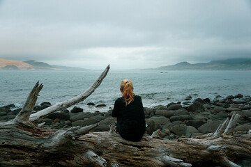 Wall Mural - A woman sitting on the rock at Waimamaku Coast in New Zealand.