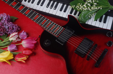 Wall Mural - Electric guitar, synthesizer keyboard and a bouquet of tulips and lilies of the valley on a red table.