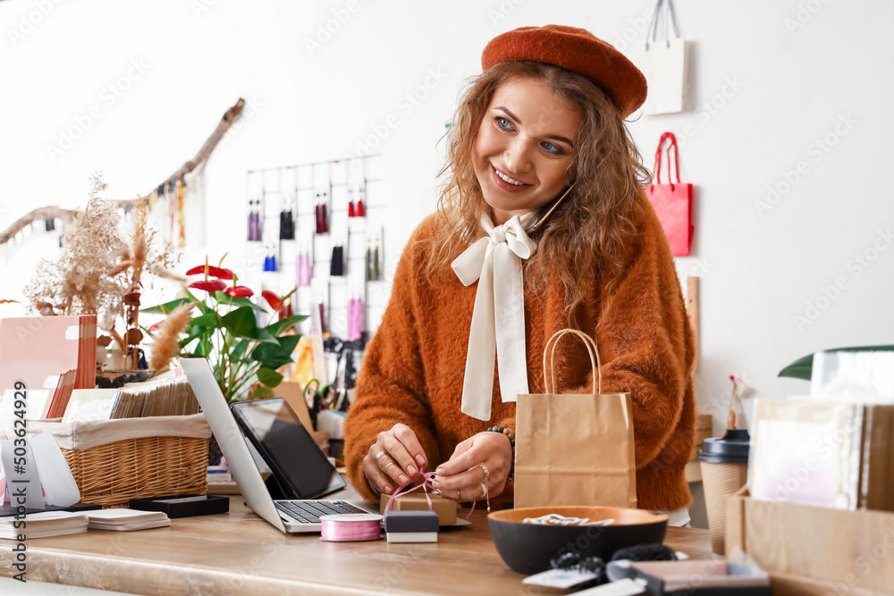 Female business owner talking by phone while packing order in shop