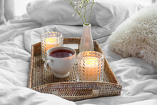 Holders With Burning Candles, Cup Of Tea And Flowers On Bed