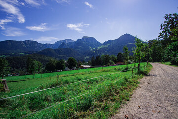 Wall Mural - Road along green meadow leading to a typical small Berchtesgaden town in Germany