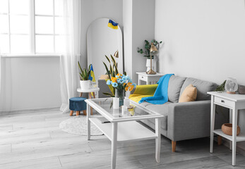 Interior of light living room with sofa, Ukrainian flags and houseplants