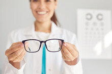 Close Up Of Smiling Woman Optician Offer Glasses Fir Client Or Customer In Optics Salon. Female Doctor Recommend Eyesight Correction Spectacles For Good Sight. Healthcare, Medicine Concept.