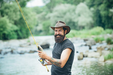 Fisherman Man On River Or Lake With Fishing Rod. Hipster Bearded Man Catching Trout Fish.
