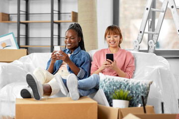 Sticker - moving, people and real estate concept - happy smiling women with smartphones and boxes at new home