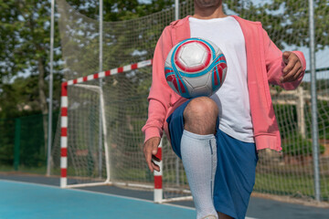 Wall Mural - Image of a man tapping the ball with his knee. Close-up image of a young boy hitting the ball with his leg on a blue soccer field with the goal in the background.