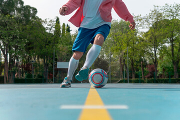 Wall Mural - Image of a man starting a dribble with the ball on the yellow line. Close-up image of a young boy with white socks and a sweatshirt doing a bicycle on a blue soccer field with the goal in the back.