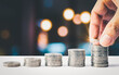 Man hand stacked coins with money saving concept and profit graph business finance in a piggy bank with money boxes for future funds of tourism, home, and retirement on a blurred background.