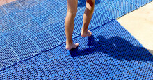 Close-up Legs Of A Little Girl Run Along The Rubber Track By The Pool. Rubber And Plastic Cover. Protection For Children By The Pool And Safety On Holiday. Healthy And Active Seaside Vacation.