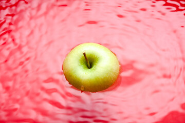 Wall Mural - Swimming apple on red background. Water surface with a swimming green apple.