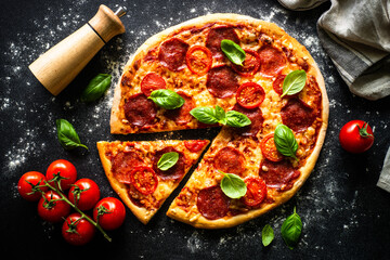 Pizza on black background. Traditional italian pizza with salami cheese, tomatoes and basil. Top view.