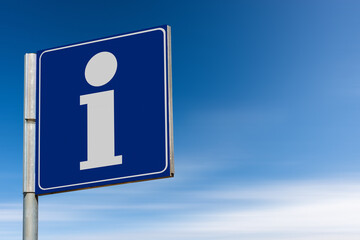 Closeup of a blue tourist information sign with the letter i against a clear blue sky with clouds and copy space. Photography.