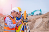 Fototapeta  - Surveyor engineer wearing safety uniform ,helmet and radio communication with equipment theodolite to measurement positioning on the construction site of the road with construct machinery background