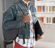 © Svyatoslav Lypynskyy - Young student african american man holding books and backpack strap wearing denim jacket. No face visible young student man on the way to school. School concept. Studies concept