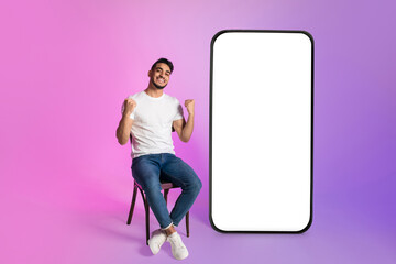 Poster - Young Arab guy offering huge smartphone with mockup, gesturing YES, advertising web store, casino or lottery app