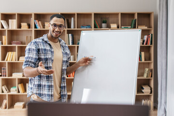 Poster - Presentation concept. Portrait of happy male manager standing near blank empty whiteboard and pointing at copy space