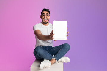 Poster - Excited millennial Arab man showing tablet with blank screen in neon light, mockup for app or website