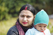 Shallow focus shot of a Southeast Asian woman with a bindi and nose piercing holding a baby in a gr