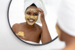 © Wavebreak Media - Smiling african american mid adult woman looking in mirror and applying face pack