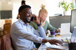 © Wavebreak Media - Cheerful african american mid adult businessman talking on smart phone while using laptop in office