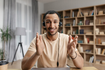 Wall Mural - Positive arab freelancer guy in headphones having online video call, speaking to business partner and gesturing at camera