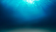 Sunlight Shining Through The Surface Of The Blue Ocean, Sea, With Dark Waters And Sandy Seabed Below.
