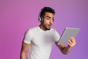 Poster - Shocked Arab guy in headphones looking at tablet screen, cannot believe his eyes, winning online lottery or casino bet