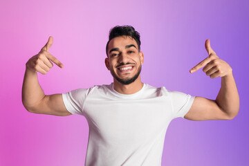 Poster - Portrait of happy millennial Arab man pointing two fingers down, offering space for your advertisement in neon light