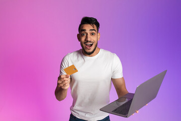 Poster - Excited young Arab man holding credit card and laptop, feeling overjoyed over huge online sale or discount in neon light
