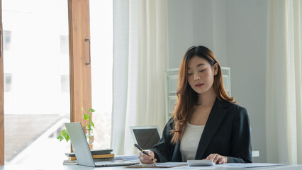 Fototapete - Young woman using a calculator and other hand using a pen take a note in the book and have notebook on the table at cafe or co working space. co working space concept.